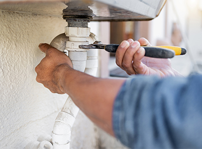 Gloved hands tightening plumbing fittings on copper pipes against a basement wall